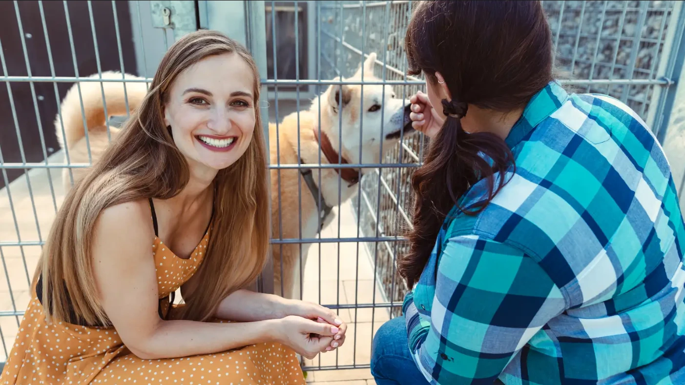 A woman sits in a cage with a dog, highlighting the emotional bond formed through shelter pet adoption.